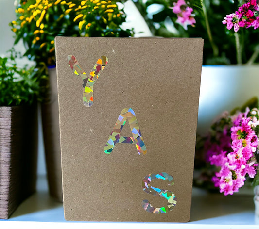 YAS HOLOGRAPHIC Greeting Card on a shelf full of colourful flowers 