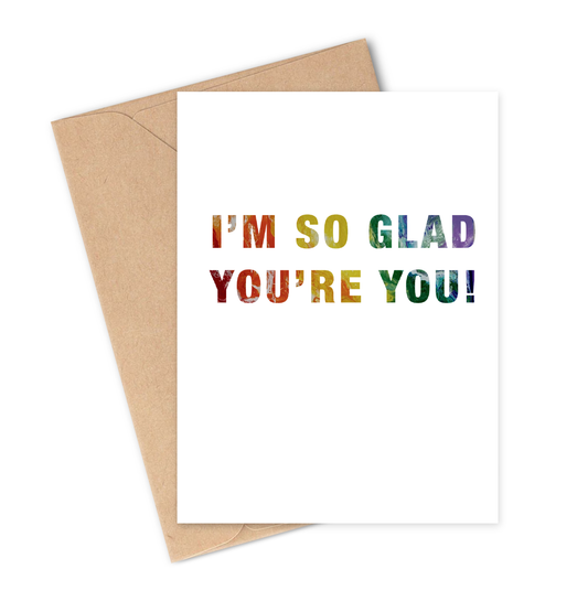Greeting card with 'I'm so glad you're you!' rainbow text on a white background with a brown envelope.