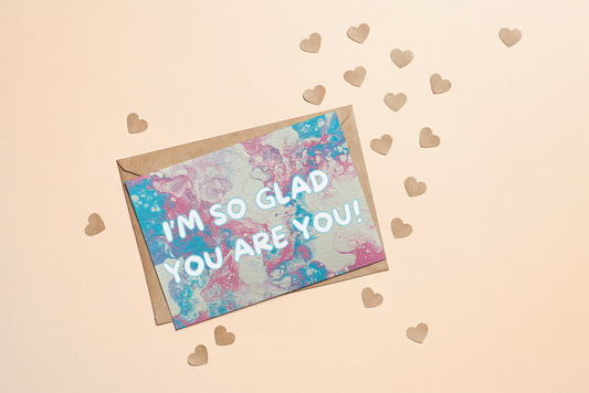 Greeting card with 'I'm so glad you are you!' text on a trans pride flag coloured background with heart shapes.